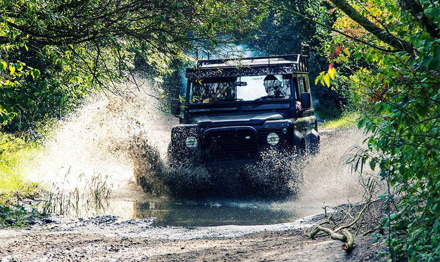 Defender 110 Een Land Rover Defender 110 die door een plas rijdt tijdens een offroad avonntuur op het terrein van ActionPlanet. - Oxtarn Clinics & Adventures