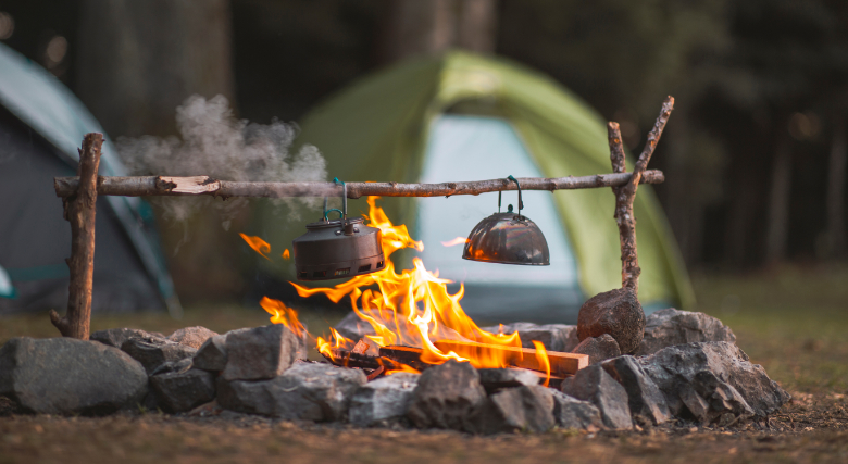 Tenten naast een kampvuur met pannen tijdens een Survival Clinic. - Oxtarn Clinics & Adventures