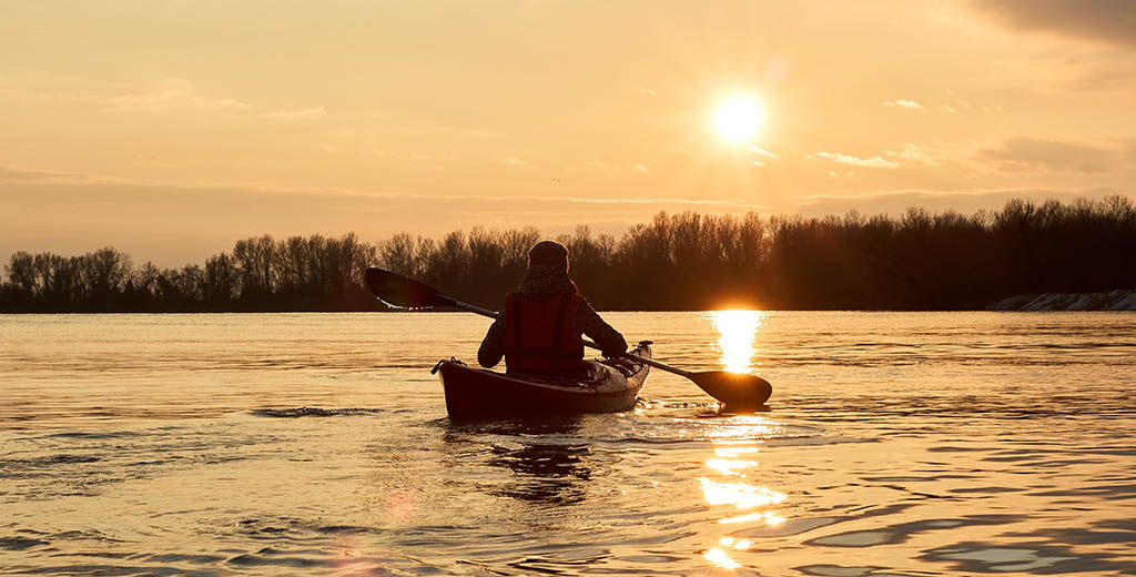 Man in kajak tijdens natuurtocht Man die geniet de natuur peddelennd in z'n kajak op een meer tijdens de zonsondergang. - Oxtarn Clinics & Adventures.