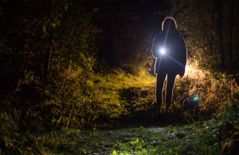 Vrouw met een zaklamp in de nacht door het bos tijdens een Oriöntatie dropping. - Oxtarn Clinics & Adventures