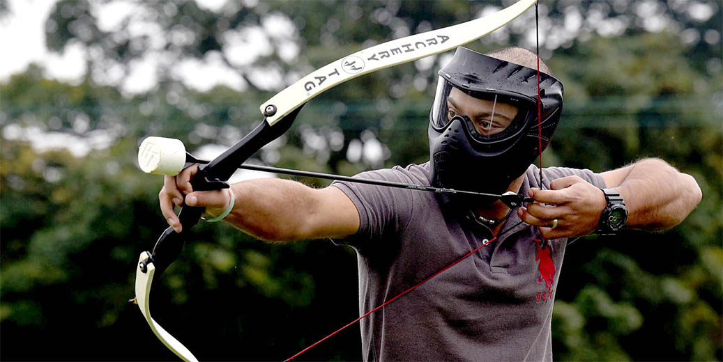 Man in het bos met masker en Archery Tag boog klaar om een team genoot af te schieten. - Oxtarn Clinics & Adventures